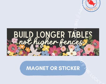 Può includere: Una calamita o adesivo rettangolare con sfondo nero e il testo bianco BUILD LONGER TABLES not higher fences. Il design è decorato con una composizione floreale colorata che include fiori rosa, rossi, gialli e blu.