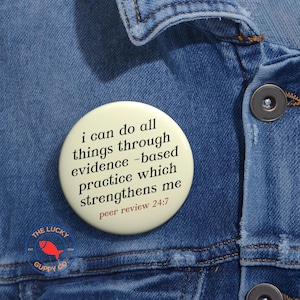 May include: A round, off-white button with the text "i can do all things through evidence-based practice which strengthens me peer review 24:7" in black and red. The button is pinned to a blue denim jacket. A small logo with a red fish is visible.