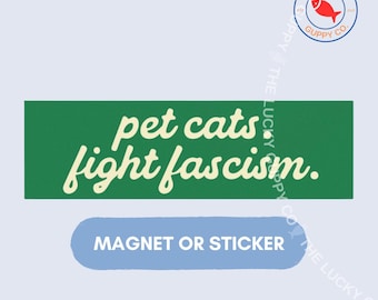 May include: A rectangular green sticker or magnet featuring the cream-coloured text pet cats fight fascism. Below the green rectangle is a light blue rounded rectangular shape containing the white text MAGNET OR STICKER.
