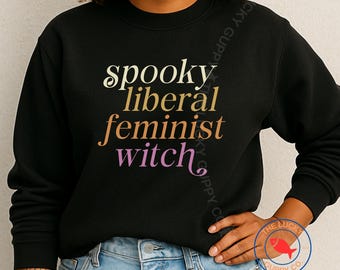 May include: Black sweatshirt with the words "spooky liberal feminist witch" in a gradient of colors. The text is in a stylized font. The Lucky Guppy Co. logo is visible on the lower right.