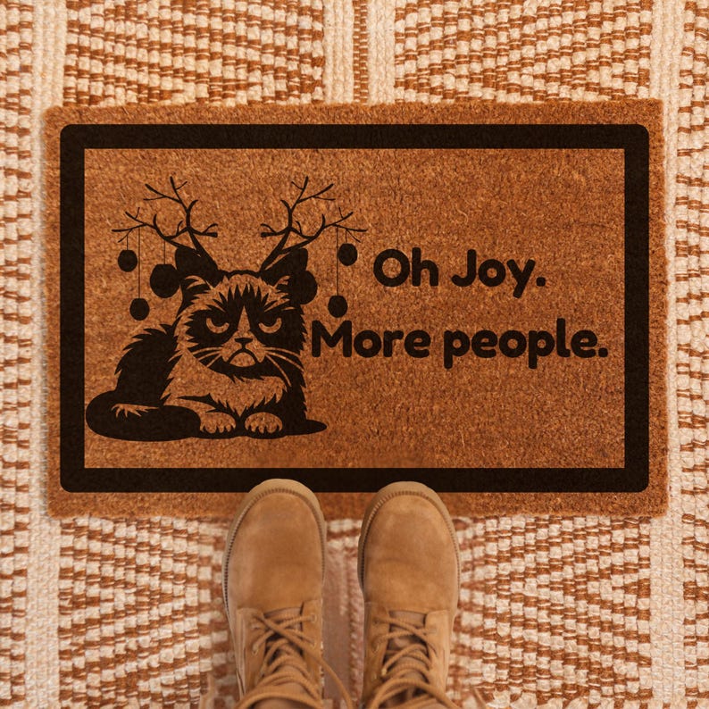 May include: A brown doormat with a black cat wearing reindeer antlers and the text "Oh Joy. More people."