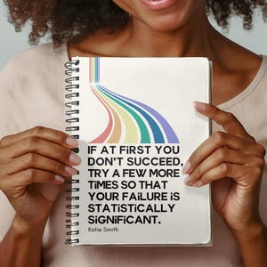 May include: A white notebook with a rainbow design and the quote "If at first you don't succeed, try a few more times so that your failure is statistically significant." by Katie Smith.