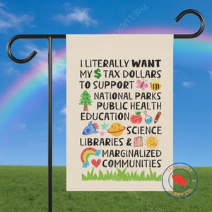 Op de afbeelding: Een tuinvaandel met de tekst "I literally want my tax dollars to support national parks, public health, education, science, libraries & marginalized communities." De vlag heeft kleurrijke illustraties.