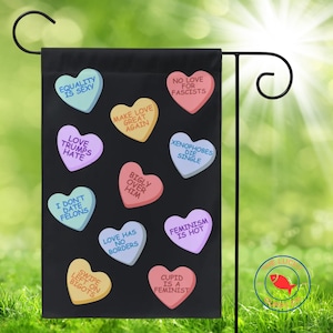 May include: Black garden flag featuring colorful candy hearts with various phrases like "Equality is Sexy" and "Love Trumps Hate." The flag is designed for outdoor use and is displayed on a metal stand in a grassy setting.