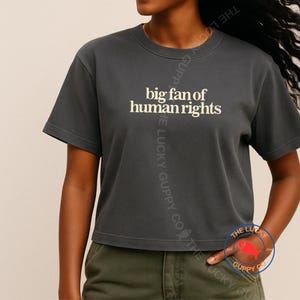 May include: Charcoal grey cropped t-shirt featuring the text "big fan of human rights" in a cream font. The top has a crew neck and short sleeves. The Lucky Guppy Co. logo is visible on the bottom right.