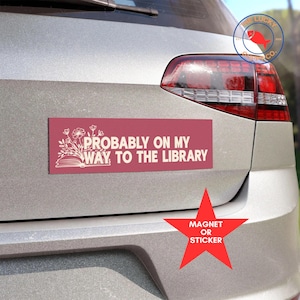 May include: A red bumper sticker with white text that reads "Probably on my way to the library". The sticker features a stylized image of a book and flowers. The sticker is on the back of a silver car. The text "Magnet or Sticker" is on a red star.