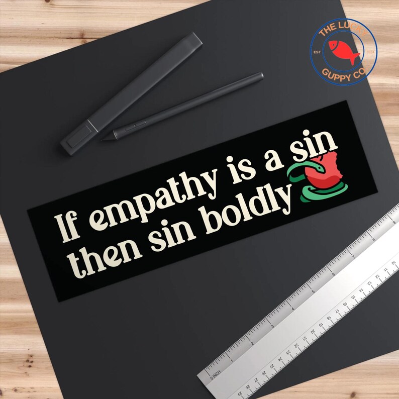 May include: Black and white sticker with the text "If empathy is a sin then sin boldly" in white font. A red and green snake with a red apple in its mouth is in the bottom right corner.