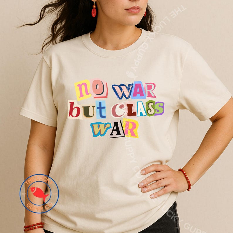 May include: Cream-colored t-shirt with the text "NO WAR but CLASS WAR" in colorful, cut-out style letters. The shirt has a crew neck and short sleeves. The Lucky Guppy Co. logo is visible.