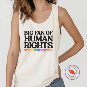 May include: Cream-colored tank top with the text "BIG FAN OF HUMAN RIGHTS" in black, with a rainbow of hearts below the text. The Lucky Guppy Co. logo is visible on the bottom right.