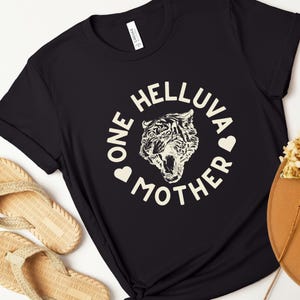 May include: Black t-shirt with a white graphic design of a tiger with the text "One Helluva Mother" in a circle around the tiger.