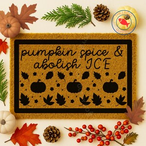 May include: A rectangular doormat with the text "pumpkin spice & abolish ICE" in black script. The mat is tan with a black border and features black pumpkin and leaf designs. Decorative fall foliage and pumpkins surround the mat.