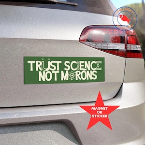 May include: Green bumper sticker with the text "TRUST SCIENCE NOT MORONS" in white with a DNA strand and an atom symbol. The sticker is on a silver car with a red star sticker that says "MAGNET OR STICKER".