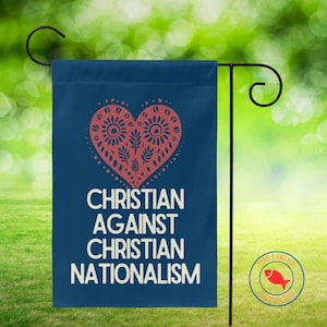 May include: A navy blue garden flag with the text "CHRISTIAN AGAINST CHRISTIAN NATIONALISM" in white. A red heart with floral designs is at the top. The flag is hanging on a black metal stand.