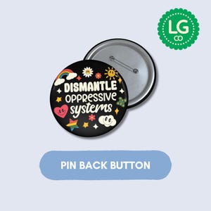 May include: A round pin back button with a black background featuring the white text "DISMANTLE OPPRESSIVE SYSTEMS" surrounded by colorful illustrations of a rainbow, a smiling heart, a star, a sun, a flower, a butterfly, and a smiling cloud.
