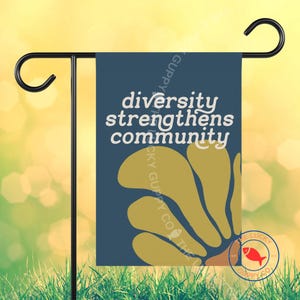 May include: A garden flag with the text "diversity strengthens community" in white on a navy blue background. A yellow floral design is at the bottom. The flag is hanging on a black metal stand.