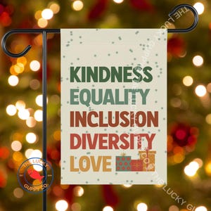 May include: A garden flag with the words "KINDNESS, EQUALITY, INCLUSION, DIVERSITY, LOVE" in green, red, and orange. The flag has a festive design with snowflakes and gift boxes. The flag is displayed on a black metal stand.