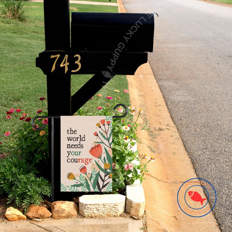 May include: Black mailbox with gold house numbers 743. A small garden flag with the text "the world needs your courage" and floral illustrations is displayed in front of the mailbox.