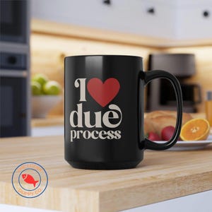 May include: Black ceramic mug with the text "I ❤️ due process" in white and a red heart. The mug has a large handle and is sitting on a wooden surface. The mug is from The Lucky Guppy Co.