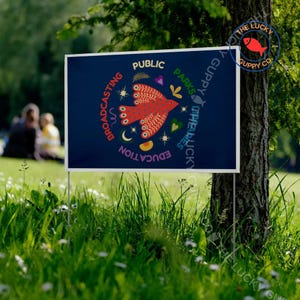 May include: A rectangular sign with a dark blue background is displayed outdoors. The sign features a red bird design with the words "PUBLIC PARKS" and "EDUCATION" in a circular arrangement. The sign is in a grassy area near a tree.