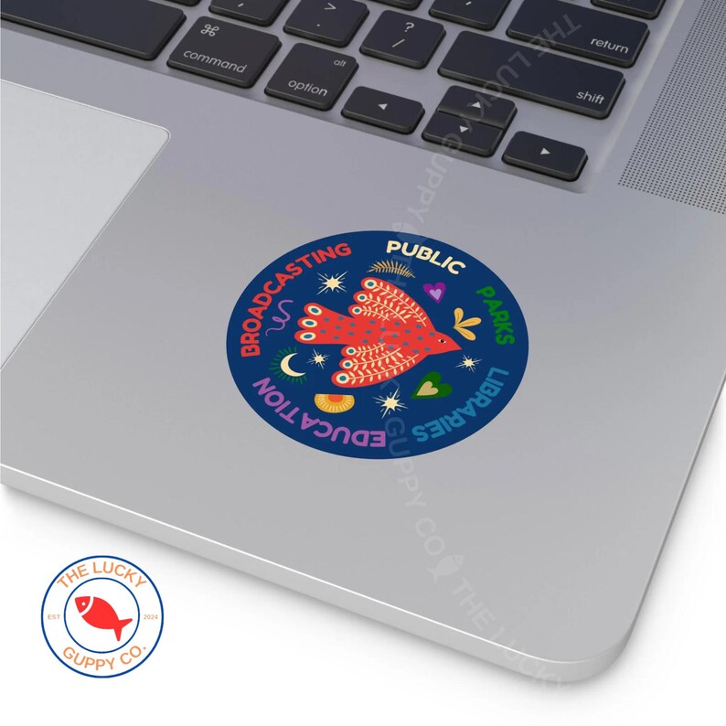Puede incluir: Una pegatina redonda con fondo azul marino. Presenta un dise&ntilde;o de p&aacute;jaro rojo y las palabras "Broadcasting, Education, Public, Parks, Libraries". Un peque&ntilde;o logotipo de un pez rojo est&aacute; en la esquina inferior izquierda.