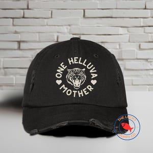 May include: Black distressed baseball cap with a white graphic of a tiger with the text "One Helluva Mother" in a circle.