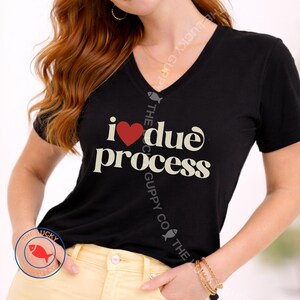 May include: Black V-neck t-shirt with the phrase "i ❤️ due process" in white and a red heart. The shirt is a short-sleeved style.