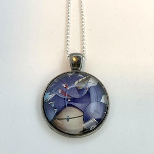 May include: A silver chain necklace with a round glass pendant featuring a cartoon illustration of a purple dragon with a red eye and a horn. The dragon is wearing a blue and white collar.