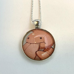 May include: A silver chain necklace with a round pendant featuring a cartoon illustration of a pink and white creature with a smiling face.