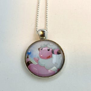 May include: A silver chain necklace with a round glass pendant featuring a cartoon image of a pink and white sheep-like Pokemon.