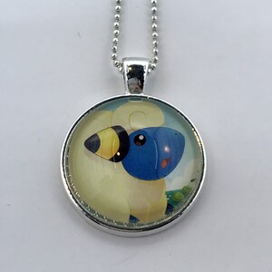 May include: A silver chain necklace with a round glass pendant featuring a cartoon illustration of a blue and yellow Pokemon character.