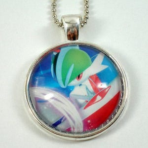 May include: A silver necklace with a round pendant featuring a colorful cartoon image of a Pokemon character with green, white, red, and blue colors.