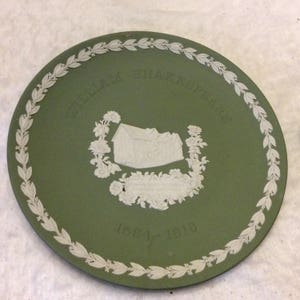 May include: A green ceramic plate with a white design of a house and a wreath. The text "William Shakespeare 1564-1616" is printed on the plate.