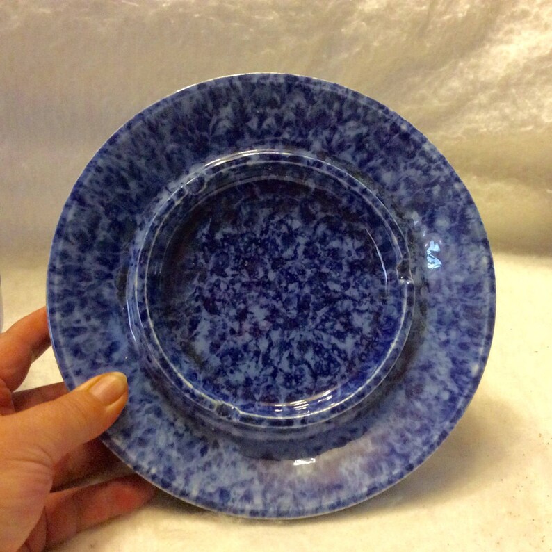 May include: Blue and white ceramic ashtray with a mottled glaze. The ashtray has a raised rim and a deep well.