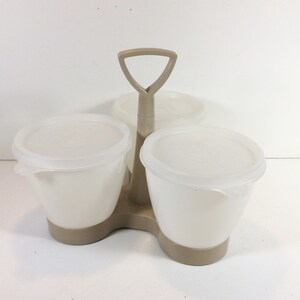 May include: A three-section beige plastic condiment holder with a handle. Each section has a white plastic bowl with a clear lid.