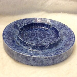 May include: A blue and white ceramic ashtray with a mottled glaze. The ashtray has a round shape with a raised center.