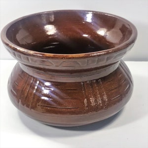 May include: A brown ceramic vase with a wide mouth and a decorative pattern around the top and bottom. The vase has a glossy finish.