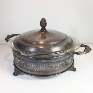 May include: Silver serving dish with a glass lid and a decorative base. The dish has a pineapple-shaped finial on the lid.