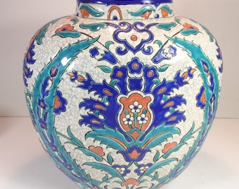 May include: A white ceramic vase with a blue, green, and orange floral pattern. The vase has a round body and a narrow neck.