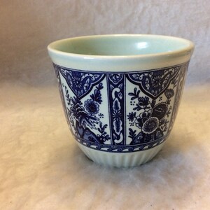 May include: A white ceramic cup with a blue and white floral pattern. The cup has a light green glaze on the inside.