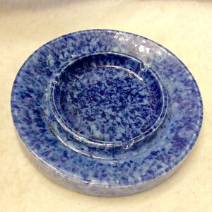 May include: A blue and white ceramic ashtray with a mottled glaze. The ashtray has a round shape with a raised rim and a center depression.