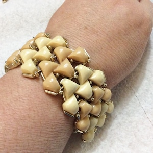 May include: A woven bracelet with a geometric pattern in shades of beige and cream. The bracelet is made of plastic and has a gold-tone clasp.