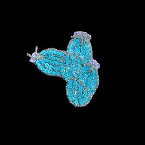 May include: A blue and purple sequined butterfly applique. The butterfly is made of small, round sequins that are sewn together to create a three-dimensional effect.