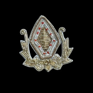 May include: A gold and silver embroidered patch with a diamond-shaped design and red beads. The patch has a floral motif and is perfect for adding a touch of elegance to clothing or accessories.