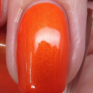 May include: Close-up of a bright orange nail polish with a glossy finish. The polish has a subtle shimmer.