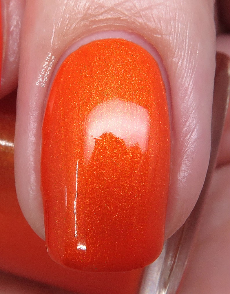 May include: Close-up of a bright orange nail polish with a glossy finish. The polish has a subtle shimmer.