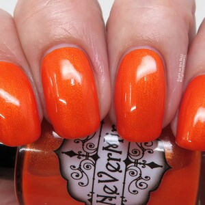 May include: Orange nail polish with a glossy finish. The bottle is labeled "The Verni", with a black and white design.