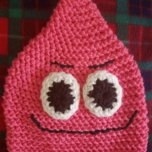 May include: Pink knitted hat with a smiling face, featuring two white eyes with black pupils and a black stitched smile.