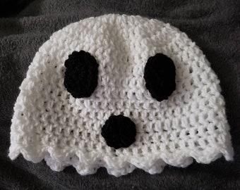 May include: A handmade white crochet hat shaped like a ghost, featuring three black circular accents for eyes and mouth. The hat has a scalloped edge, giving it a whimsical appearance. The hat is designed for Halloween or costume wear.