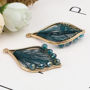 May include: A pair of gold-toned earrings with a teardrop shape. Each earring features a green tassel-like design and a row of iridescent green beads.