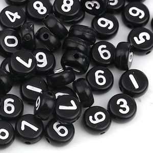 May include: Black plastic number beads with white numbers from 0 to 9. The beads are round and have a hole in the centre for stringing.